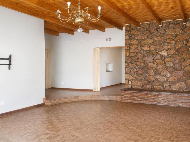 Spacious living area featuring a rustic stone accent wall, exposed timber beam ceiling, and classic parquet flooring with a raised platform section.