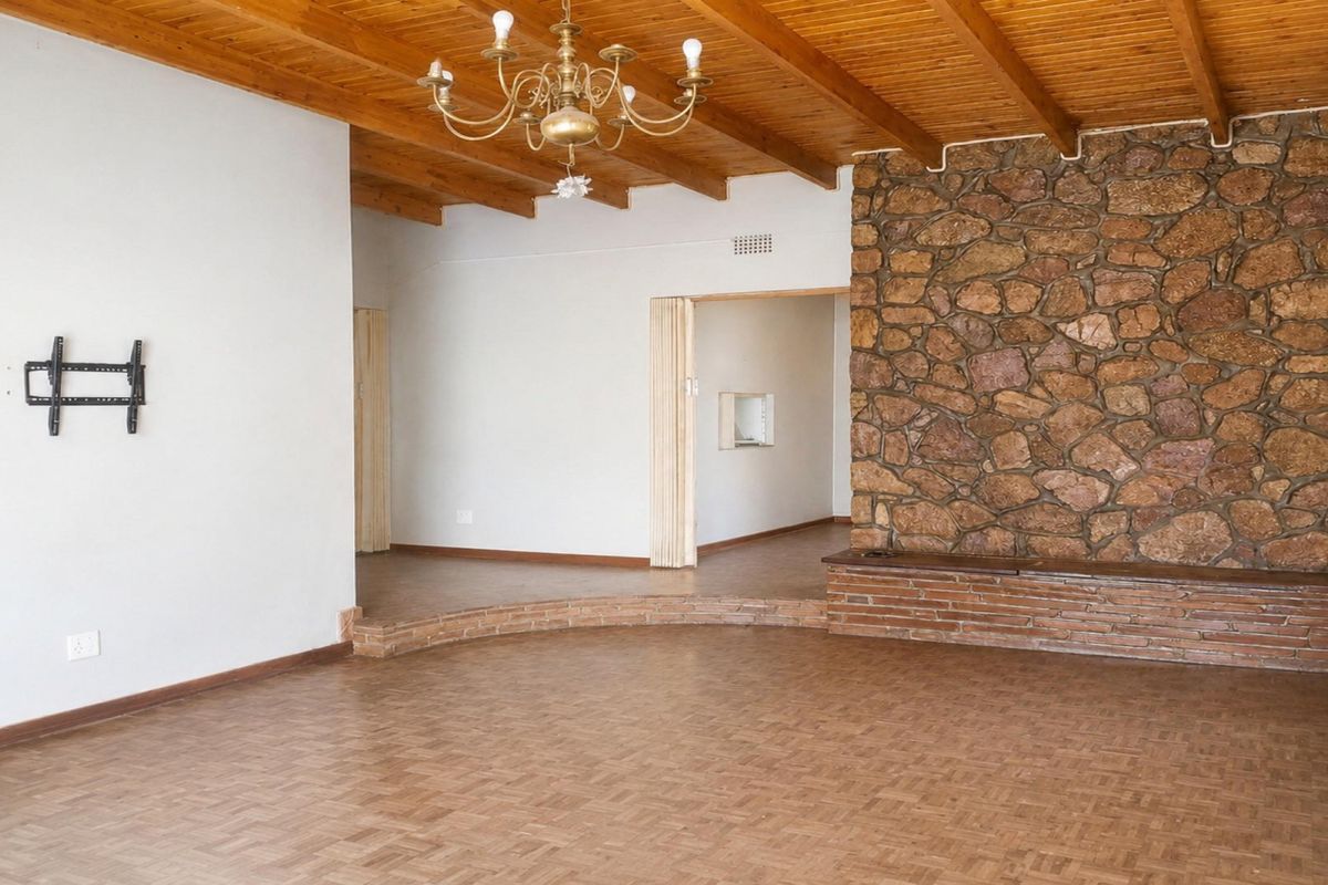 Spacious living area featuring a rustic stone accent wall, exposed timber beam ceiling, and classic parquet flooring with a raised platform section.