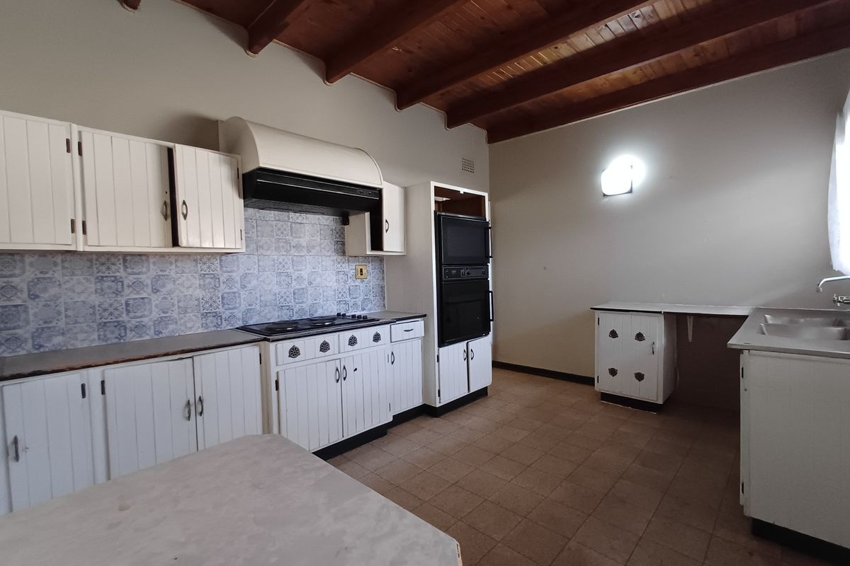 Spacious kitchen featuring exposed timber beam ceilings, built-in cabinetry, integrated oven, and tiled splashback, offering a functional layout ready for modernization.