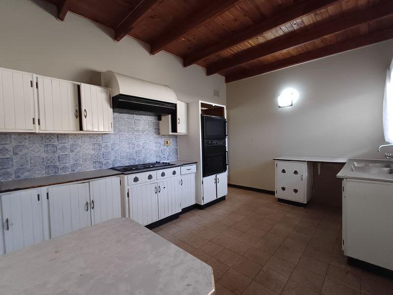 Spacious kitchen featuring exposed timber beam ceilings, built-in cabinetry, integrated oven, and tiled splashback, offering a functional layout ready for modernization.