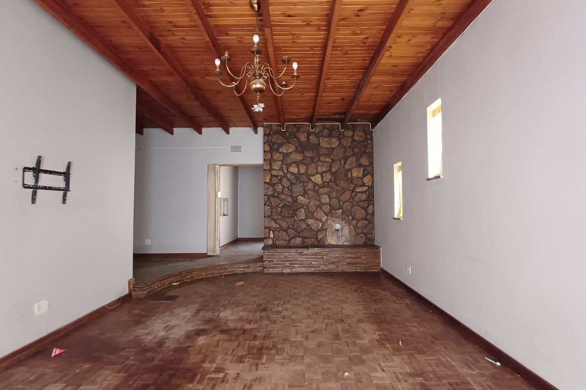 Spacious living room featuring a rustic stone fireplace, exposed timber beam ceiling, and parquet flooring, offering a character-filled space ready for renovation.