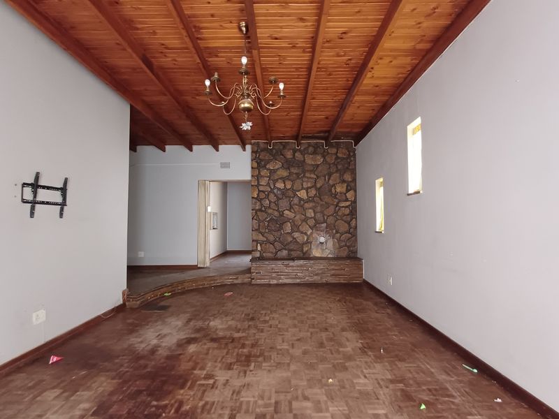 Spacious living room featuring a rustic stone fireplace, exposed timber beam ceiling, and parquet flooring, offering a character-filled space ready for renovation.