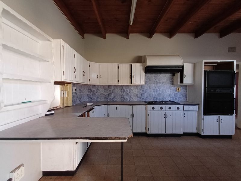 Spacious kitchen featuring white cabinetry, built-in oven, hob, extractor fan, and exposed timber beam ceiling, offering a functional layout ready for modern updates.
