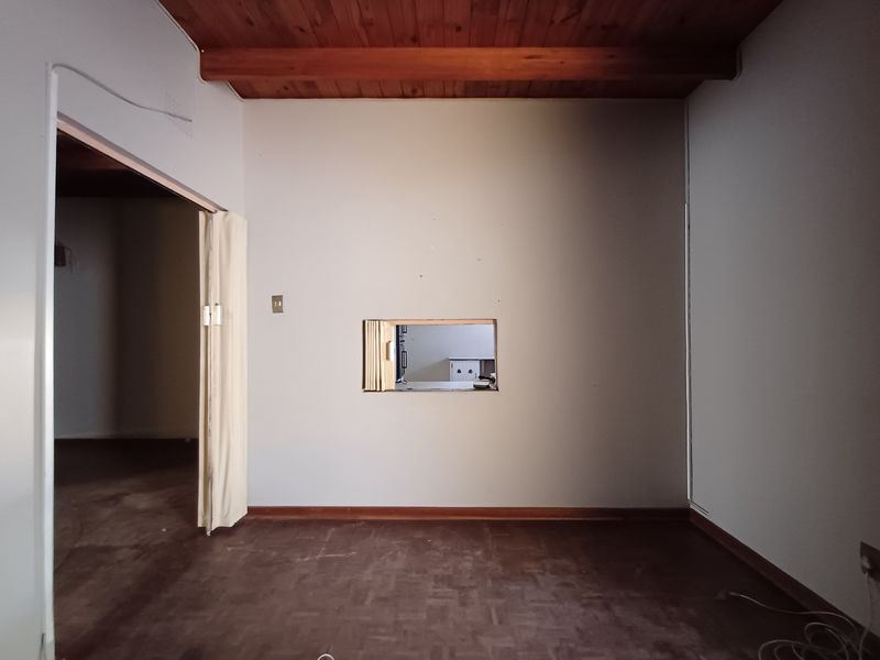 An empty living room featuring exposed timber ceiling beams, parquet flooring, and a convenient serving hatch connecting to the adjacent kitchen area.