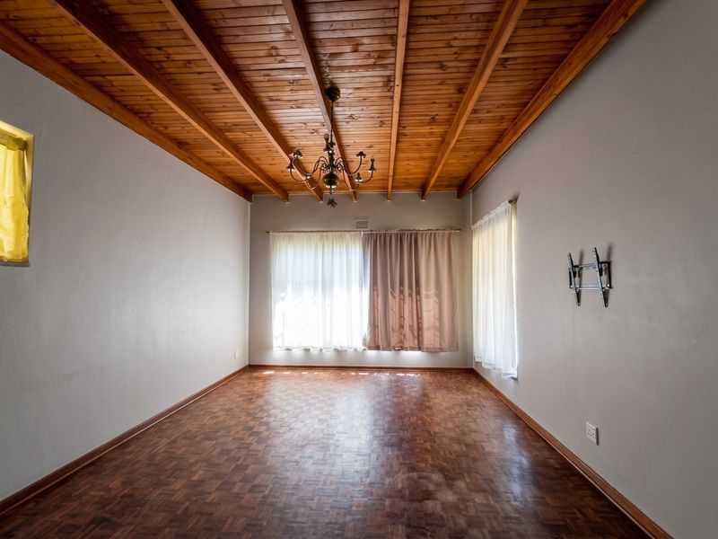 Spacious living room featuring classic parquet flooring, a distinctive exposed timber beam ceiling, and a central wrought iron chandelier.