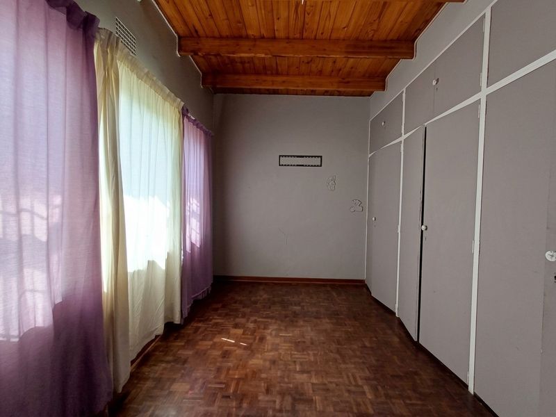 An empty bedroom featuring parquet flooring, exposed timber ceiling beams, and built-in cupboards, offering a blank canvas for personalization.