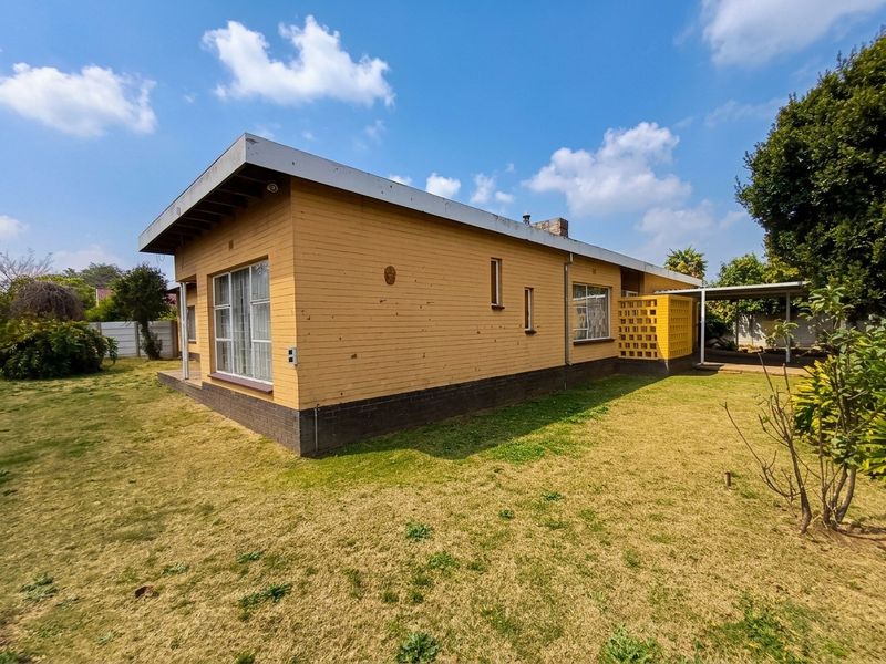 Rear view of a single-story brick house featuring a flat roof, aluminum windows, and an attached carport with a decorative breeze block wall.