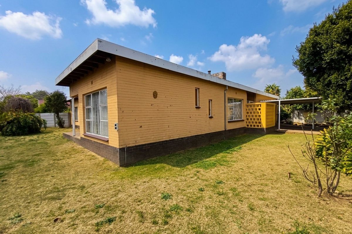 Rear view of a single-story brick house featuring a flat roof, aluminum windows, and an attached carport with a decorative breeze block wall.