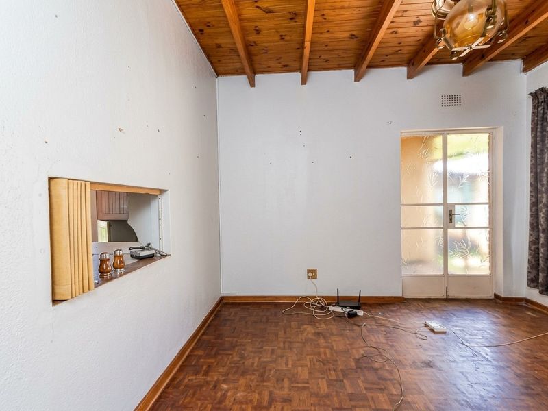 An empty living room featuring exposed timber beam ceilings, parquet flooring, and a convenient serving hatch connecting to the kitchen area.