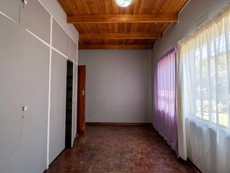 An empty bedroom featuring parquet flooring, exposed timber ceiling beams, and built-in cupboards, offering a blank canvas for renovation.