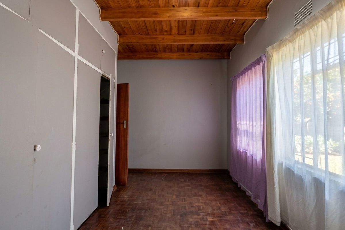 An empty bedroom featuring parquet flooring, exposed timber ceiling beams, and built-in cupboards, offering a blank canvas for renovation.