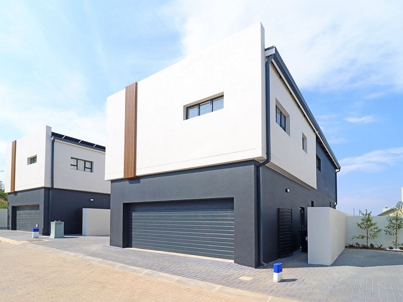 Modern double-storey residential property featuring a sleek two-tone facade, integrated double garage, and paved driveway in a contemporary estate setting.