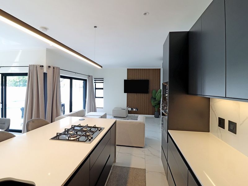 Modern open-plan living area featuring a sleek kitchen with stone countertops, gas hob, and seamless flow to the lounge with feature wall paneling.