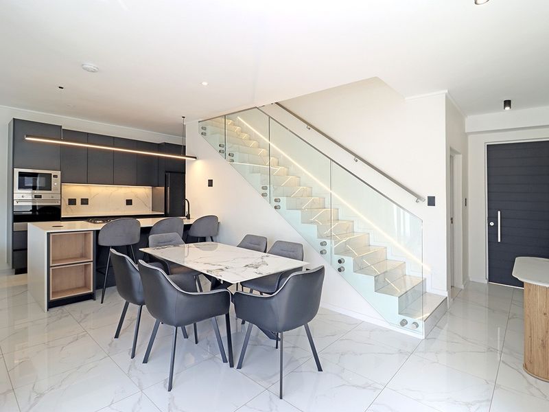 Modern open-plan living area featuring a sleek kitchen with integrated appliances, a marble-topped island, and a contemporary staircase with a glass balustrade.