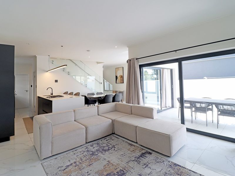 Modern open-plan living area featuring a sleek kitchen island with gas hob, glass staircase balustrade, and large sliding doors leading to the patio.
