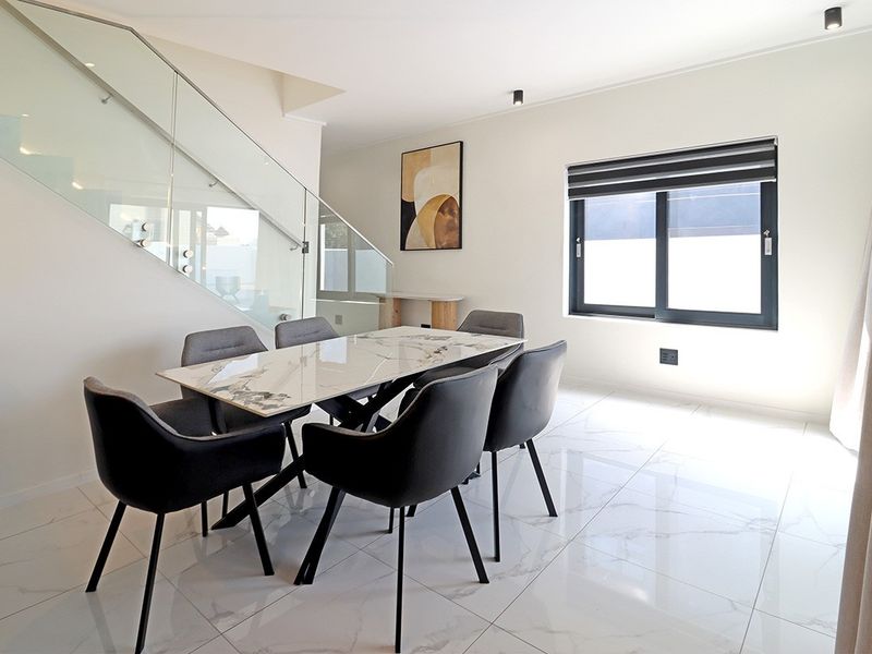 Modern dining area featuring sleek porcelain tile flooring, a contemporary glass balustrade staircase, and clean minimalist finishes.