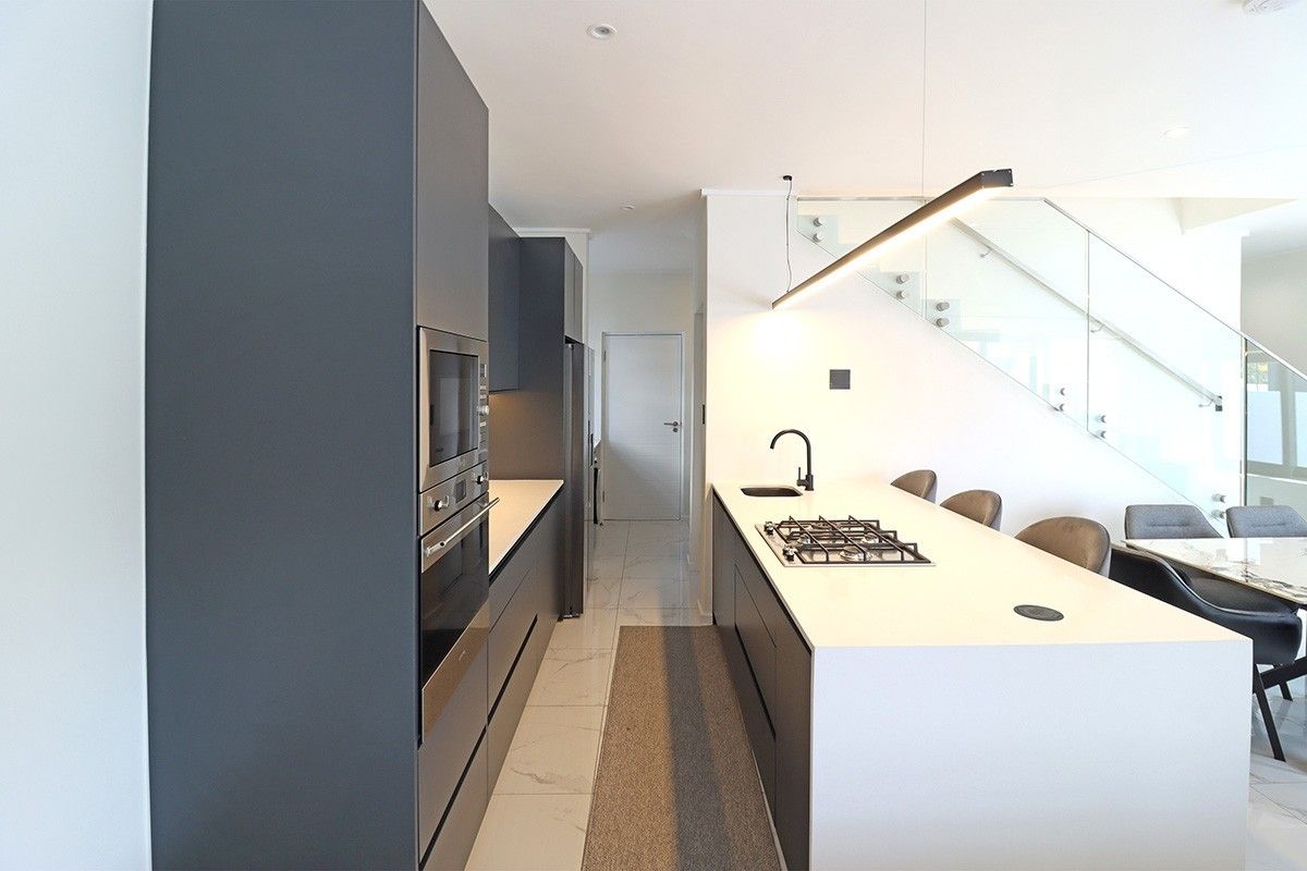Modern kitchen featuring a central island with gas cooktop, integrated appliances, sleek cabinetry, and an adjacent glass-railed staircase in an open-plan layout.