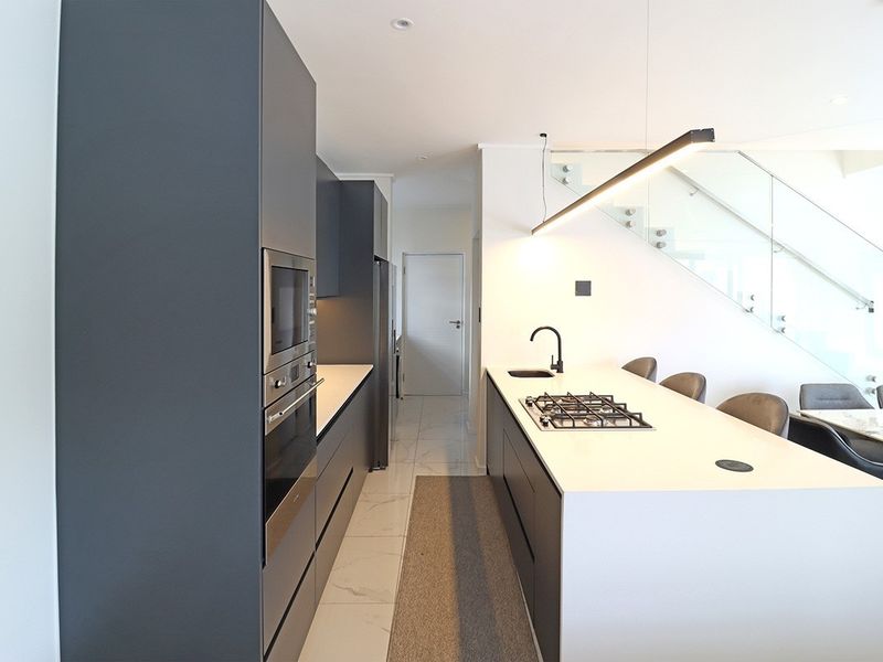 Modern kitchen featuring a central island with gas cooktop, integrated appliances, sleek cabinetry, and an adjacent glass-railed staircase in an open-plan layout.