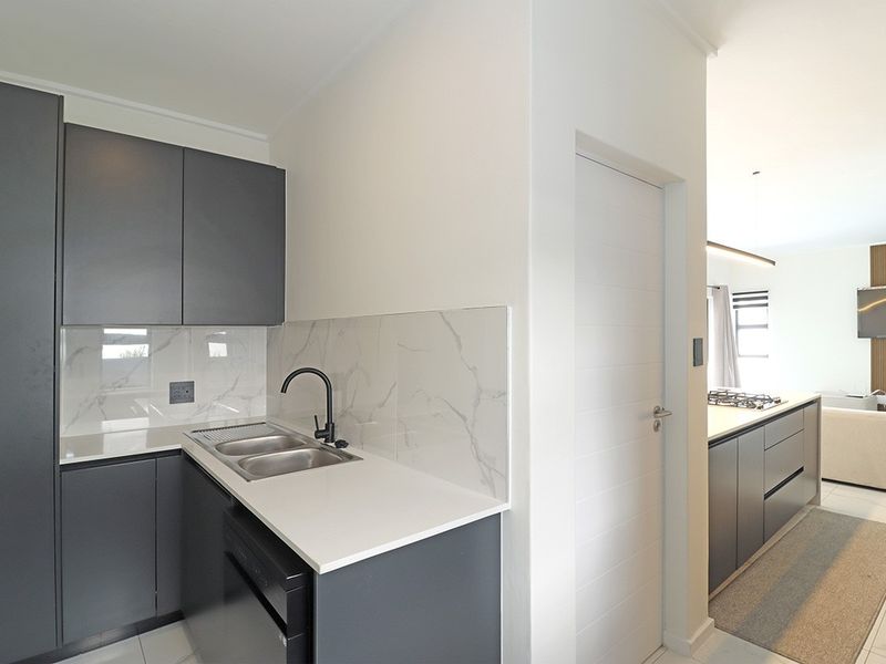 A modern, well-appointed scullery featuring dark grey cabinetry, stone countertops, a double sink with a matte black mixer tap, and marble-look splashback tiling.