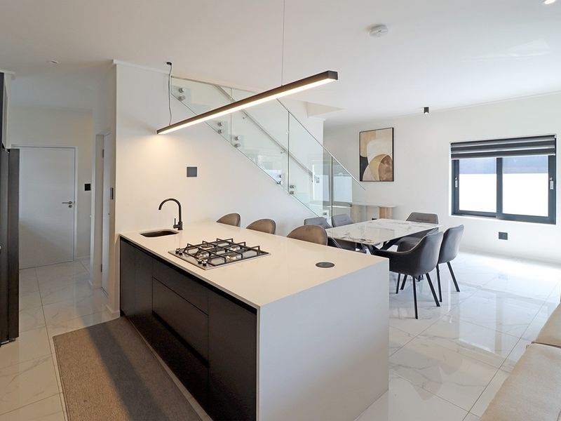 Modern open-plan living area featuring a sleek kitchen island with gas hob, marble-look floor tiles, and a contemporary glass staircase balustrade.