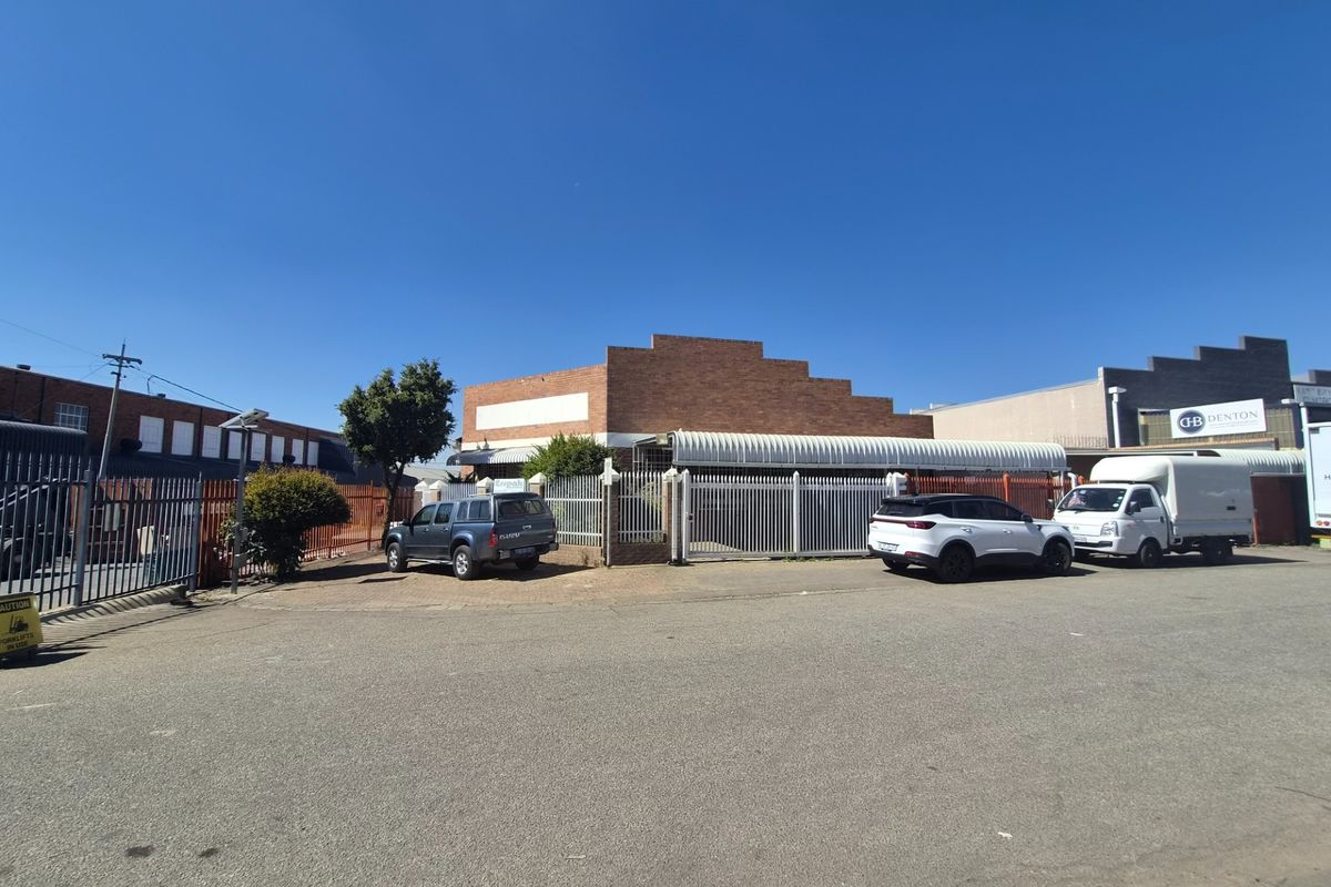 Front exterior view of an industrial property featuring a brick facade, metal security fencing, and a paved driveway area.
