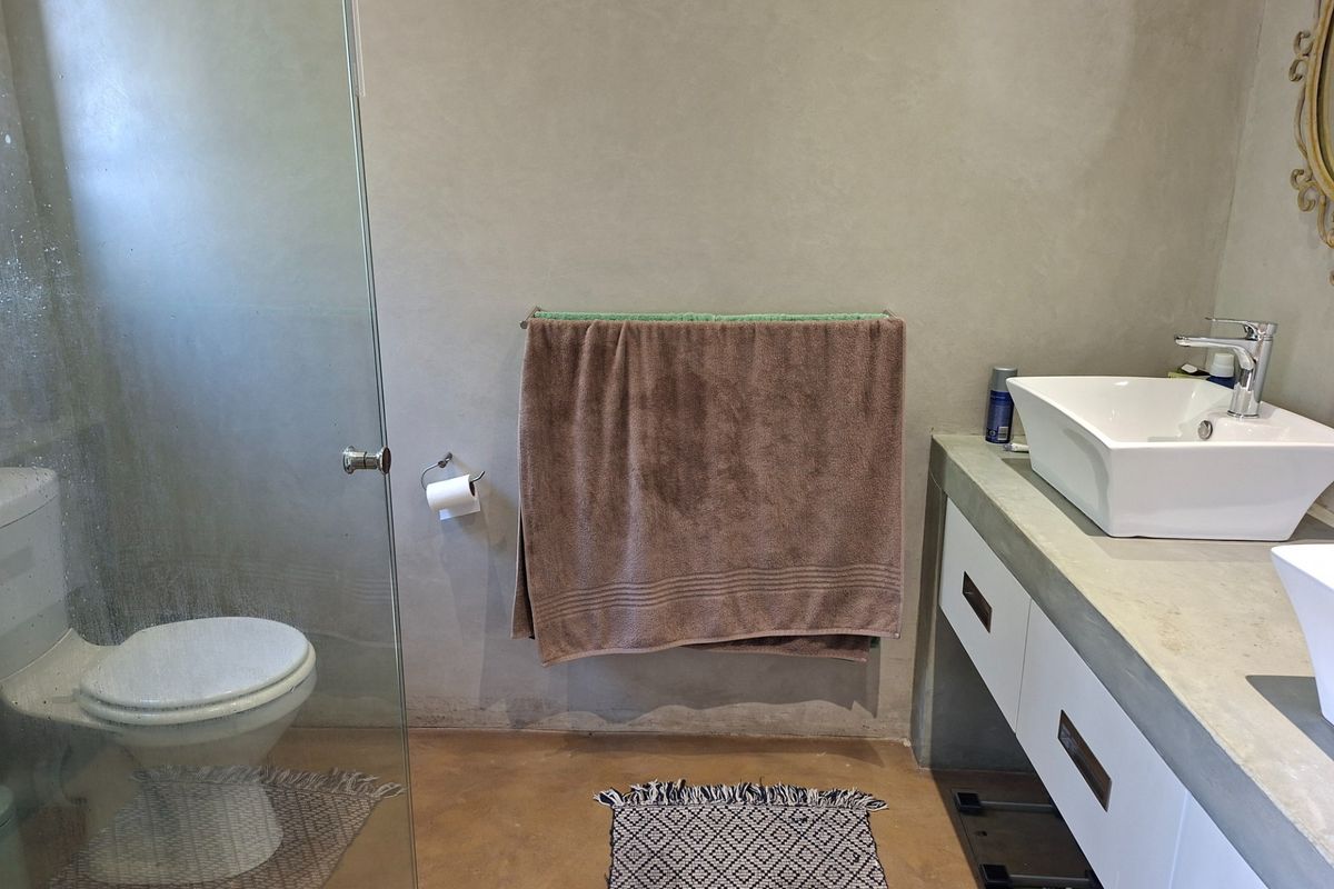 Modern bathroom featuring a concrete vanity with vessel sinks, a glass-enclosed shower, and polished concrete flooring.
