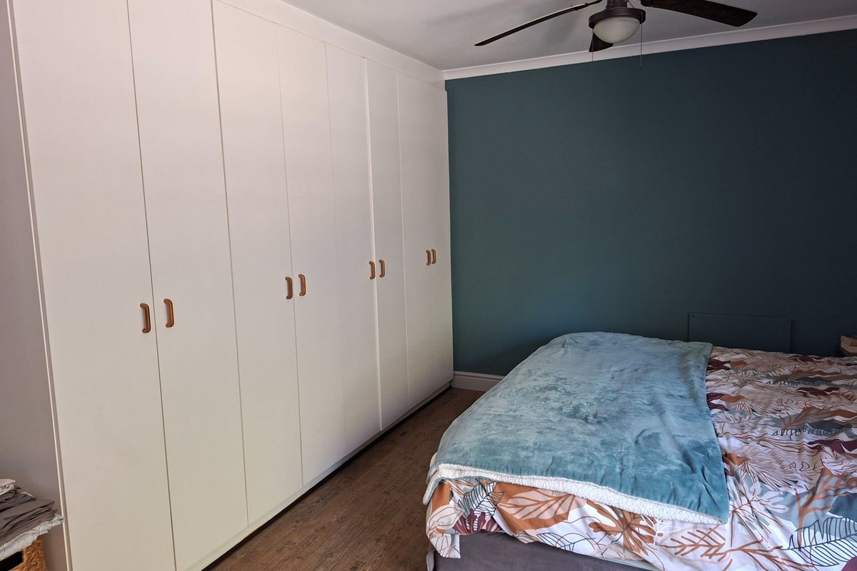 A well-maintained bedroom featuring extensive floor-to-ceiling built-in cupboards, a ceiling fan, and modern laminate flooring with a feature wall.