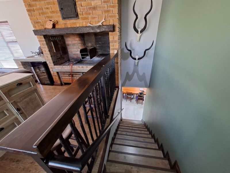 A view looking down a staircase featuring a brick fireplace and wooden handrail, overlooking a lower level dining area.