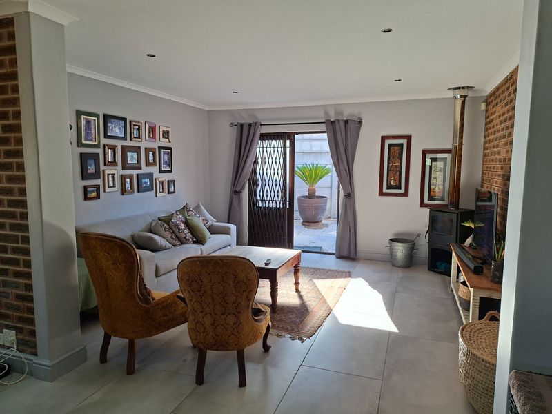 A comfortable living room featuring large floor tiles, an exposed brick feature wall, and a built-in fireplace, with direct access to an outdoor patio area.