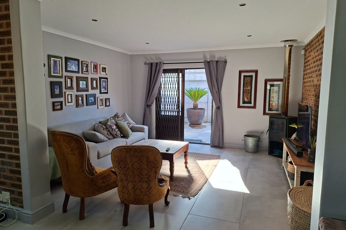A comfortable living room featuring large floor tiles, an exposed brick feature wall, and a built-in fireplace, with direct access to an outdoor patio area.
