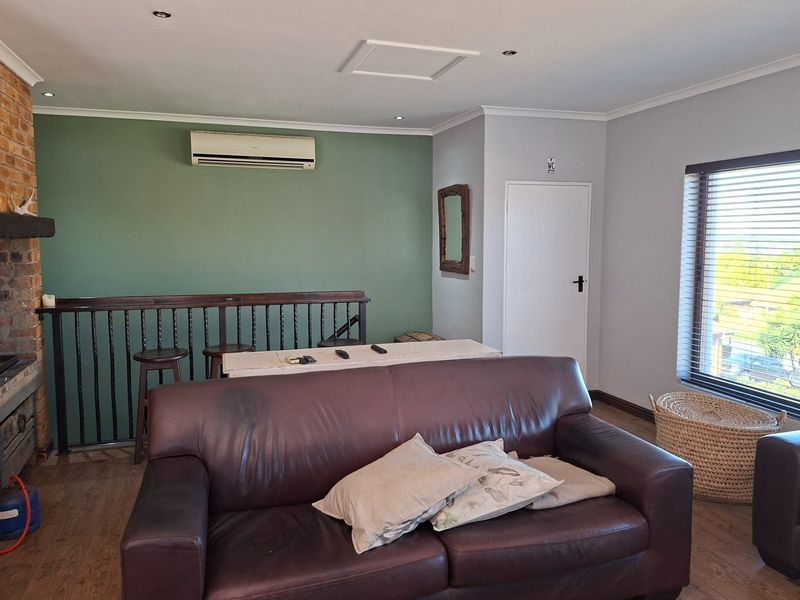 A living room featuring a brick fireplace, wooden balustrade, and wall-mounted air conditioning unit, with neutral wall tones and wood-look flooring.