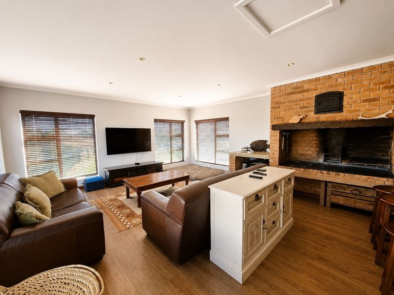 Spacious living room featuring a prominent built-in brick fireplace, laminate flooring, and large windows with venetian blinds, creating a warm and inviting atmosphere.