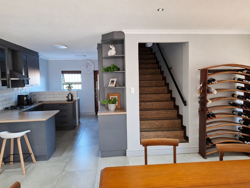 Modern open-plan kitchen featuring dark cabinetry, subway tile backsplash, and a wooden staircase leading to the upper level.