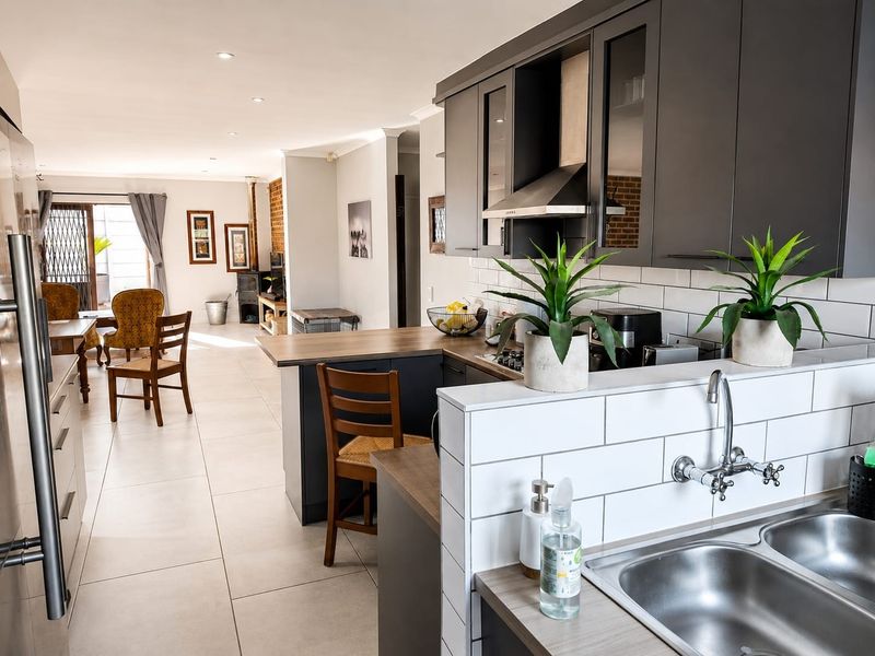 Modern open-plan kitchen and living area featuring dark cabinetry, subway tile backsplash, double sink, and a cozy wood-burning stove in the lounge.