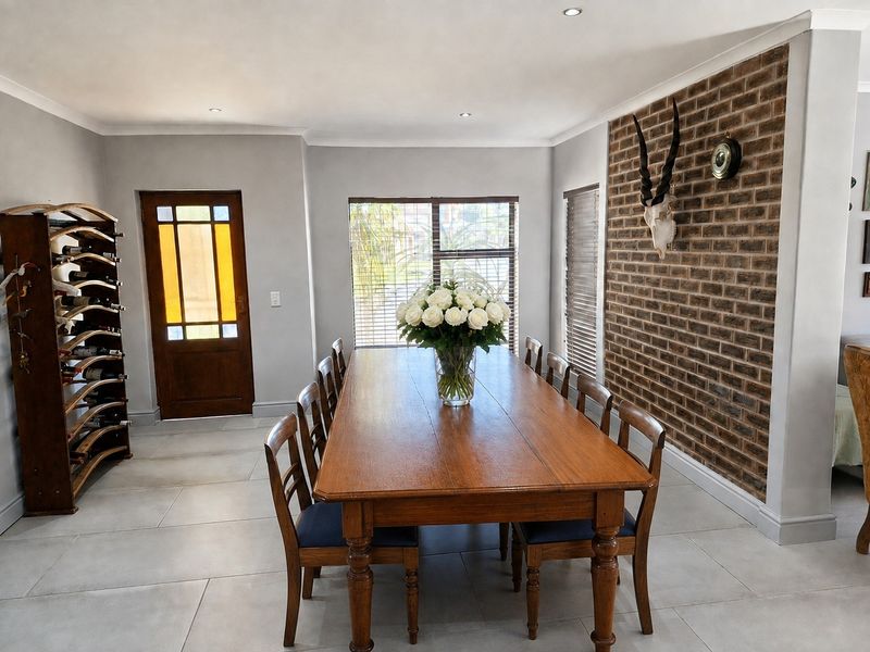 Spacious dining room featuring a prominent exposed brick feature wall, large format floor tiles, and natural light through timber-framed doors and windows.