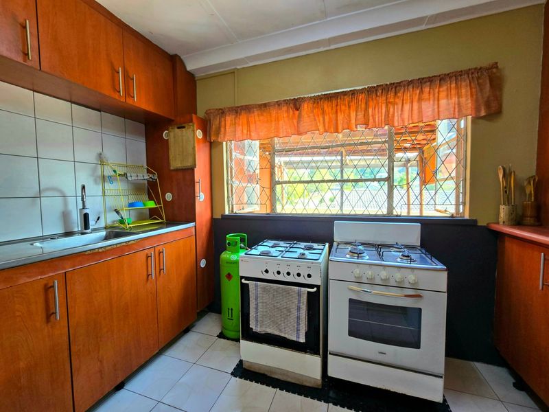 A functional kitchen featuring wooden cabinetry, tiled backsplash, stainless steel sink, and a combination gas and electric stove setup.