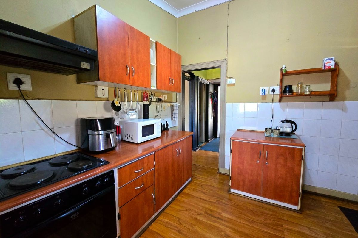 A functional kitchen featuring wood-look laminate cabinetry, electric stove with extractor, tiled backsplash, and laminate flooring, requiring cosmetic updates to modernize the space.