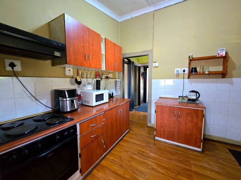 A functional kitchen featuring wood-look laminate cabinetry, electric stove with extractor, tiled backsplash, and laminate flooring, requiring cosmetic updates to modernize the space.