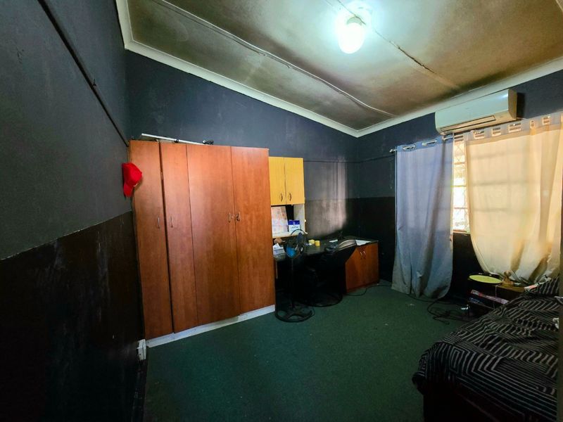 A bedroom featuring built-in cabinetry, a split-system air conditioner, and carpet flooring. The room requires cosmetic updates, including ceiling repairs and fresh paint.