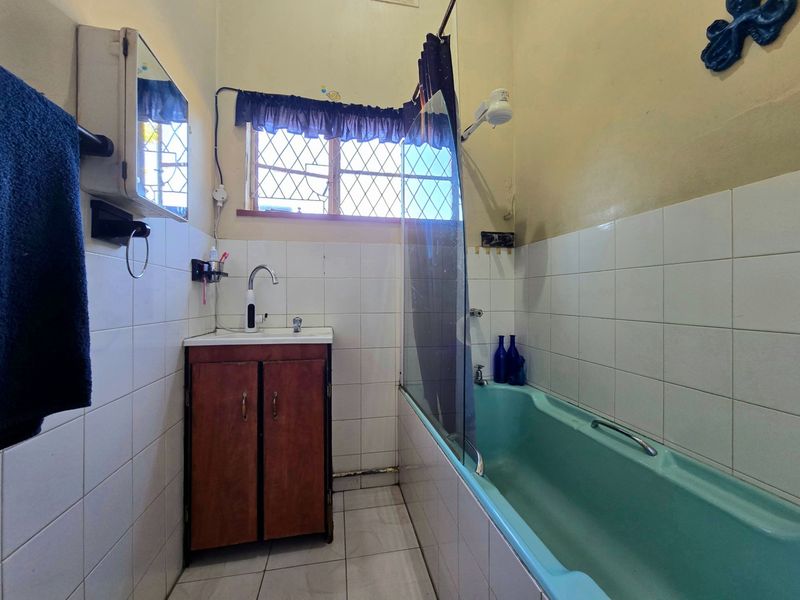 A functional bathroom featuring a bathtub with a shower screen, a vanity basin, and tiled walls and flooring.