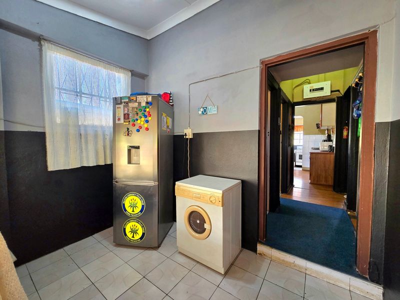 A functional laundry area featuring tiled flooring and security bars on the window, providing direct access to the adjacent kitchen space.