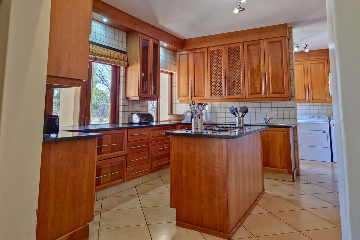 A spacious kitchen featuring warm wooden cabinetry, granite countertops, a central island with a gas hob, and tiled flooring throughout.