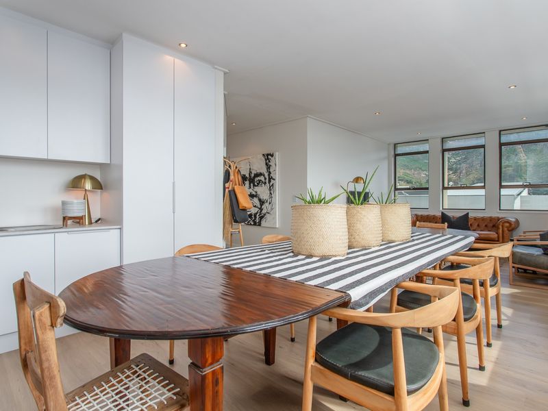 An open-plan living and dining area featuring modern built-in cabinetry, light laminate flooring, and large windows providing natural light and mountain views.