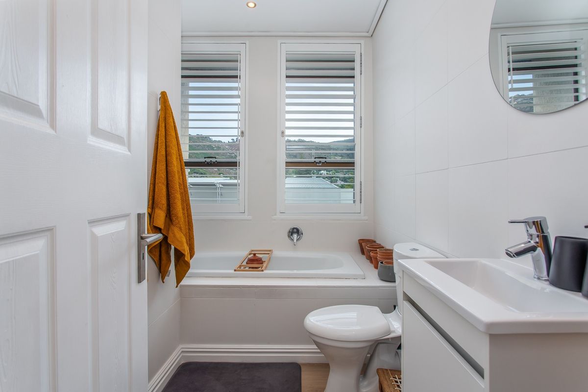 A clean, modern bathroom featuring a built-in bathtub, white vanity basin, and window shutters with natural light.