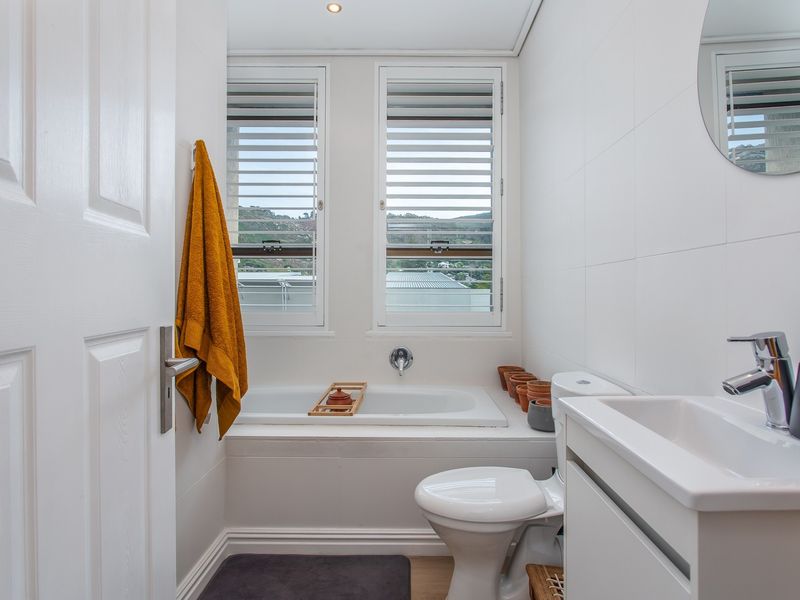 A clean, modern bathroom featuring a built-in bathtub, white vanity basin, and window shutters with natural light.