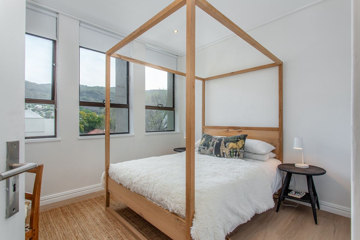 A bright and modern bedroom featuring laminate flooring, recessed lighting, and large windows with roller blinds offering natural light and views.