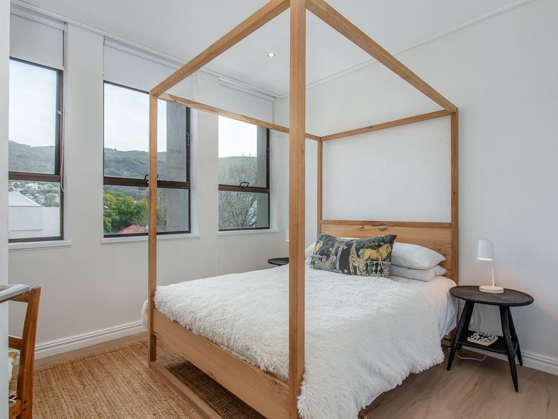 A bright and modern bedroom featuring laminate flooring, recessed lighting, and large windows with roller blinds offering natural light and views.