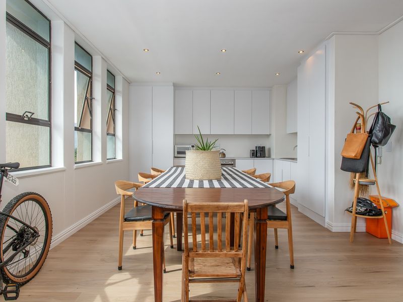 A bright open-plan kitchen and dining area featuring modern white cabinetry, recessed lighting, and light wood-look laminate flooring.