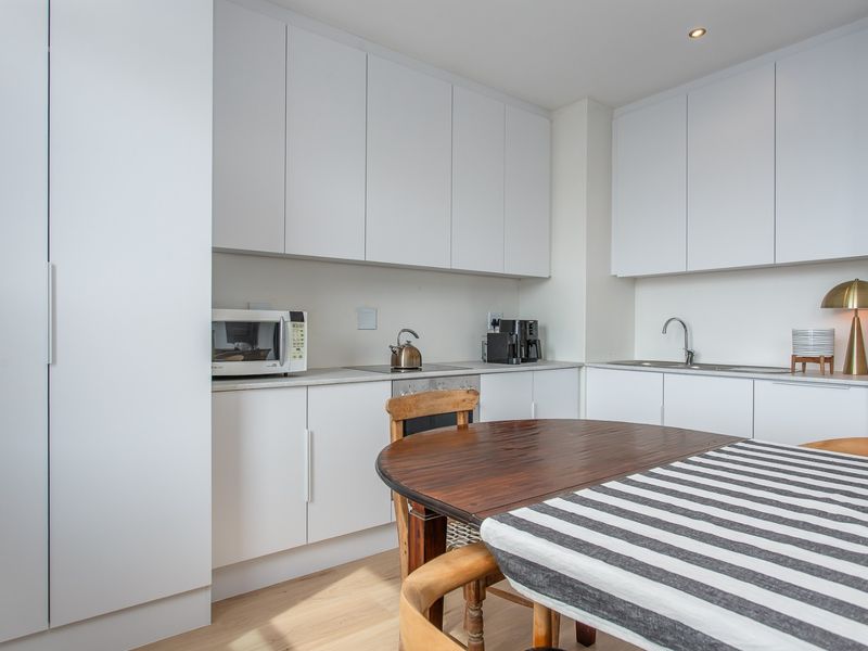 Modern kitchen featuring clean white cabinetry, integrated appliances, stainless steel sink, and light wood-look flooring in a bright, functional layout.