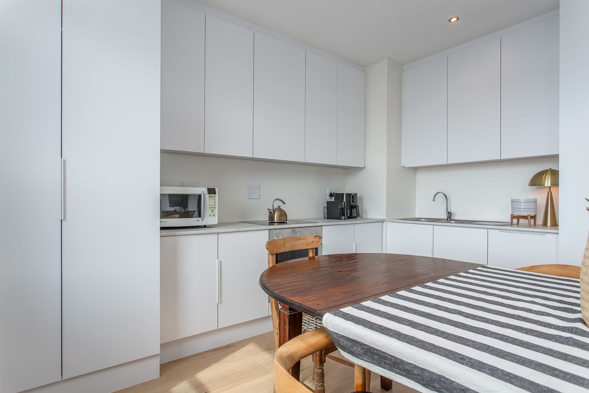 Modern kitchen featuring clean white cabinetry, integrated appliances, stainless steel sink, and light wood-look flooring in a bright, functional layout.